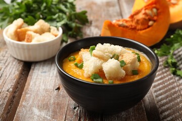Tasty pumpkin cream soup with croutons and green onion in bowl on wooden table, closeup