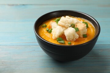 Tasty pumpkin cream soup with croutons and green onion in bowl on light blue wooden table, closeup. Space for text