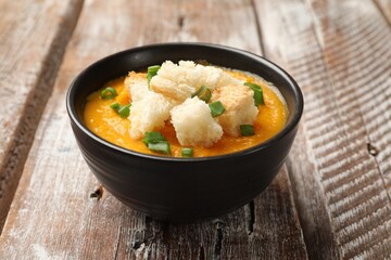 Tasty pumpkin cream soup with croutons and green onion in bowl on wooden table, closeup