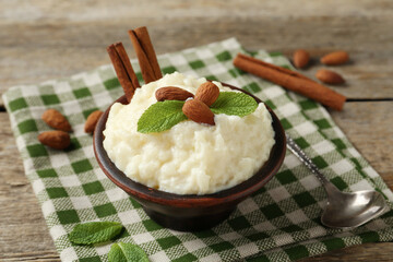 Delicious rice pudding with almonds, mint and cinnamon sticks served on wooden table, closeup