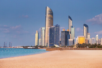 Modern skyscrapers reflecting on calm sea at sunset from Corniche beach, Abu Dhabi, United Arab...