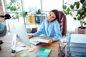 Professional woman multitasking in modern office, managing work tasks with computer and clipboard,...