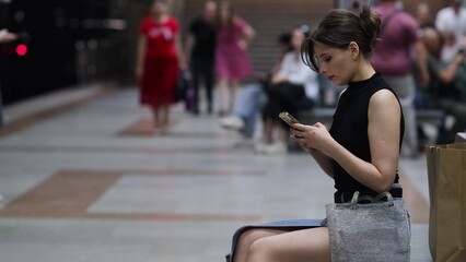 Stylish young woman reading a text message on her mobile phone while waiting for a subway train.