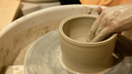 Potter shaping a clay bowl on a wheel in a studio during an evening pottery class