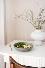 This nutritious dish features green vegetables of tomatoes and aragula, including peas and omelet elegantly presented on white table with elegant vase.
