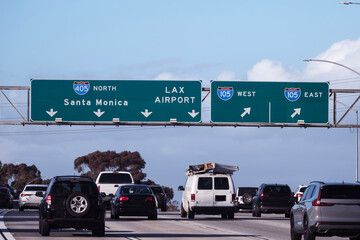 Slow traffic driving below freeway signs on the San Diego 405 freeway near LAX and the 105 freeway interchange in Los Angeles. 