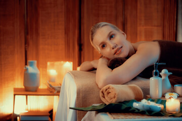 Caucasian woman customer enjoying relaxing anti-stress spa massage and pampering with beauty skin recreation leisure in warm candle lighting ambient salon spa at luxury resort or hotel. Quiescent