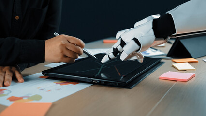 A human and a robot engage in a collaborative design process, using a touchscreen tablet to merge technology with creativity in a modern workspace.Noogenesis