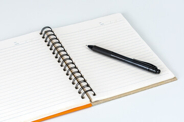 The Pen and the blank page: A sleek black pen lies on a fresh, open notebook, a symbol of creativity and the act of documenting thoughts on white background.