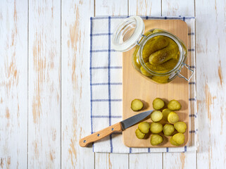 pickled cucumbers in a jar on a white wooden table, top view.