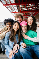 Naklejka premium Vertical photo of diverse group of happy young students sitting together at city street. Youth community and international friendship concept