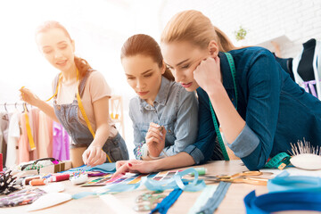 Fototapeta premium Three girls at garment factory. They are choosing colors for new dress.