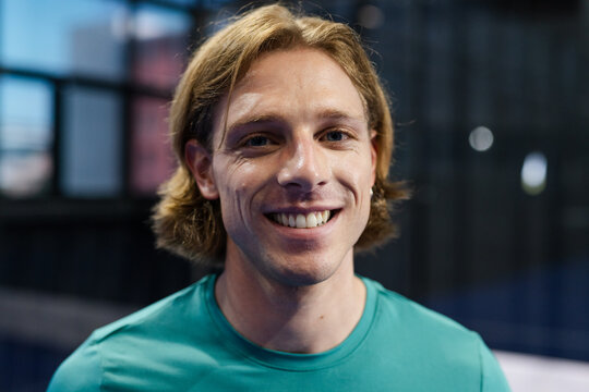 Smiling man in teal shirt enjoying padel tennis indoors, feeling confident and happy - Powered by Adobe