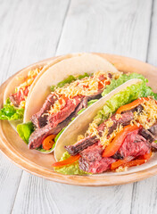 Three carne asada tacos filled with steak, grilled peppers, lettuce, and cheese