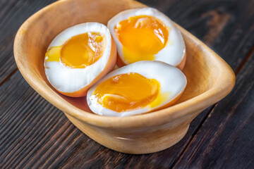 Halved ajitsuke tamago ramen eggs with golden yolks in wooden bowl
