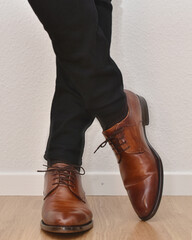 a man stands in black trousers and brown leather shoes