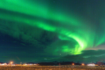 Fototapeta premium Beautiful Aurora Borealis over house on the island of Kvaløya, dancing northern lights with green light, red and purple strikes, clear colored rays of light in the sky, amazing joy in Norway