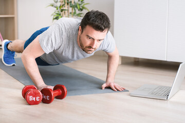 Man doing exercise while watching tutorial on laptop at home