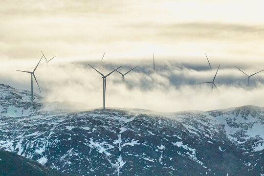 wind park in fog on the snowy mountains from the island of Kvaløya, Norway, with many wind turbines in clouds. amazing windmills in winter on the coast of the Atlantic produce electricity.