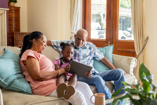 African American grandparents and granddaughter using tablet on living room sofa - Powered by Adobe
