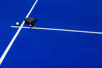 Padel racket and ball resting on blue court, ready for match, copy space