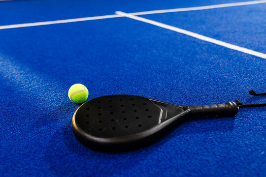 Padel racket and ball resting on blue court, ready for action