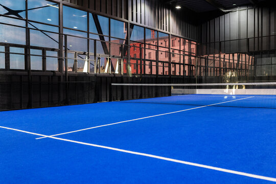Empty indoor padel tennis court with blue flooring and glass walls, copy space
