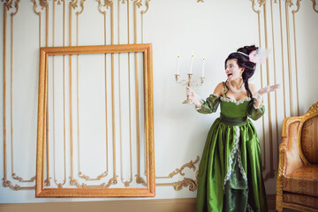 Elegant woman in a historical green dress holding a candelabra in a classic baroque setting with...