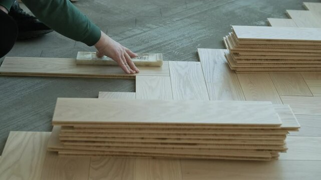Worker installing wooden flooring with hammer and tapping block