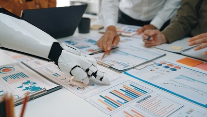 A business meeting scene featuring a robotic hand actively engaging with various charts and graphs, symbolizing the integration of technology in collaborative environments.Noogenesis