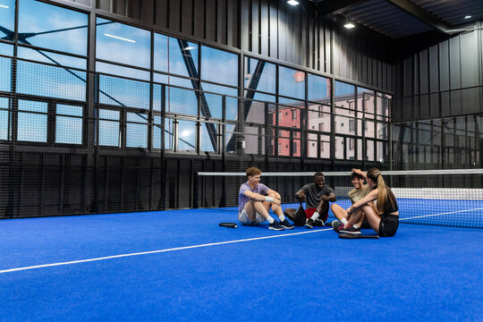 Group of friends sitting on padel court, relaxing after fun game, copy space