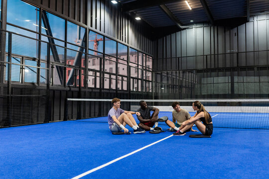 Group of friends sitting on padel court, relaxing after match, enjoying conversation, copy space