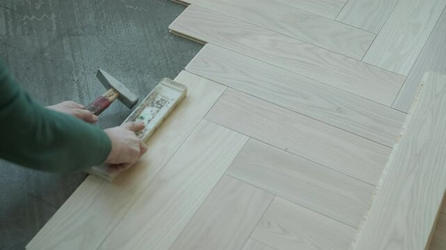 Worker installing wooden flooring with hammer and tapping block