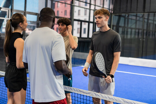 Group of young adults discussing padel tennis strategy on indoor court - Powered by Adobe