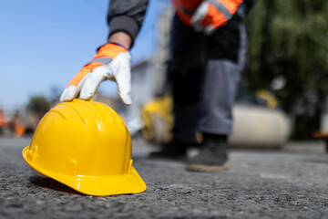 Construction worker placing a yellow hard hat on the ground in an urban setting during daylight...
