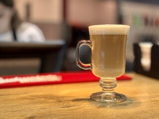 Savoring a Delicious Latte Crafted in a Clear Glass While Relaxing on a Wooden Table. A beautifully crafted latte served in a clear glass, presenting delicious layers of coffee and froth