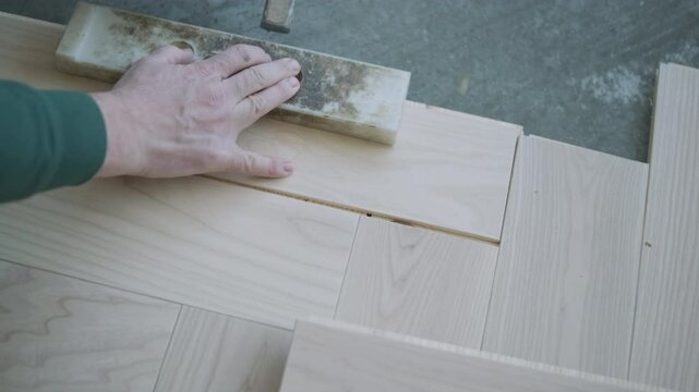 Worker installing wooden flooring with hammer and tapping block