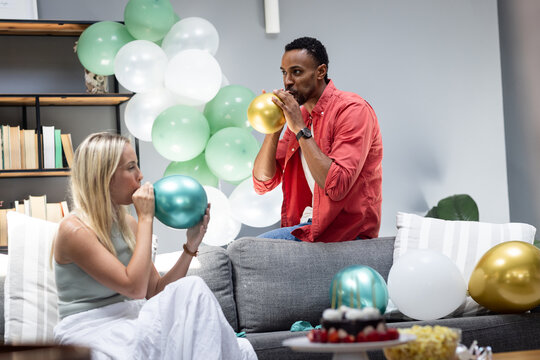 Inflating balloons for party, diverse friends preparing festive decorations at home