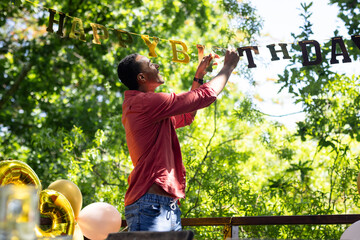 Man decorating in garden space with birthday banner, preparing for party