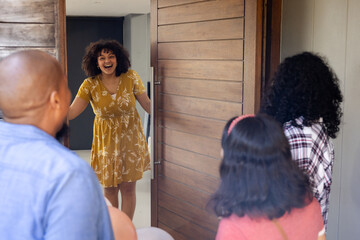 At party, African American woman welcoming diverse friends at home, smiling and opening door