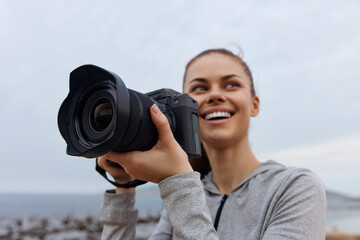 Happy young woman holding a camera on a cloudy beach, excited to capture beautiful moments during her photography adventure