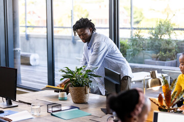 Diverse team collaborating in modern office, man arranging books near potted plant