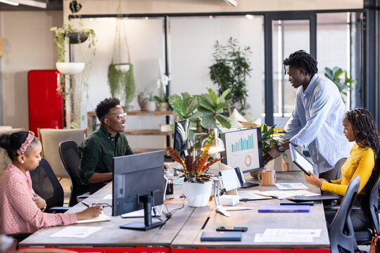 Discussing project in modern office, diverse team collaborating with charts on computer screen