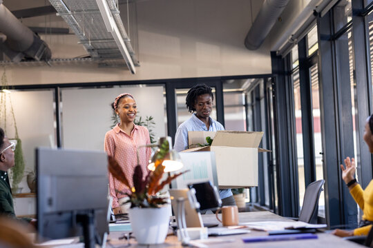 Diverse colleagues welcoming new diverse team member carrying box in modern office workspace