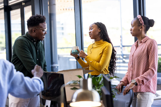 Unpacking box and holding coffee mug, diverse colleagues discussing project in modern office