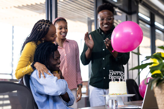 In office, celebrating birthday with diverse colleagues clapping around cake and balloons