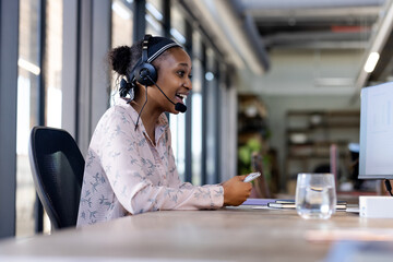 Smiling woman wearing headset working at office desk, engaging in conversation