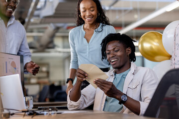 Smiling diverse team celebrating success in modern office with charts on computer screen