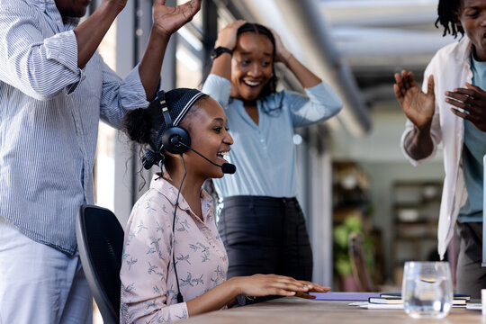 Diverse team celebrating success as woman in headset achieves milestone at office