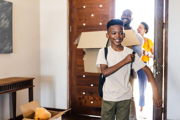 Family moving into new home, smiling boy carrying backpack, parents holding boxes